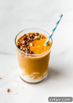 a pumpkin pie smoothie topped with granola with a striped blue and white straw in it