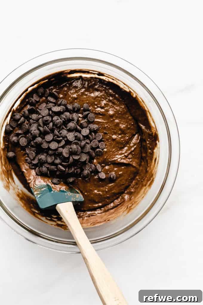 Wholesome Chocolate Pumpkin Delight 6 A mixing bowl of decadent chocolate pumpkin bread batter, generously adorned with dark chocolate chips on the surface, ready for the final fold.