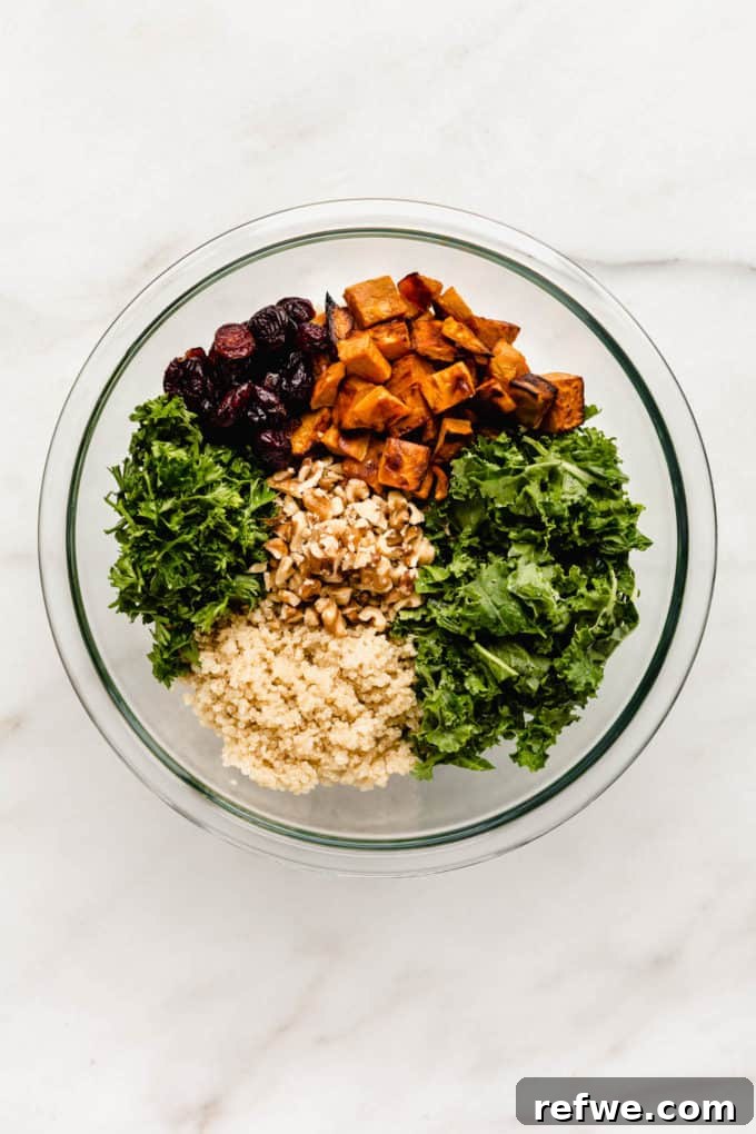A clear mixing bowl filled with fresh kale, cooked quinoa, parsley, sweet potatoes, cranberries, and walnuts, ready to be tossed