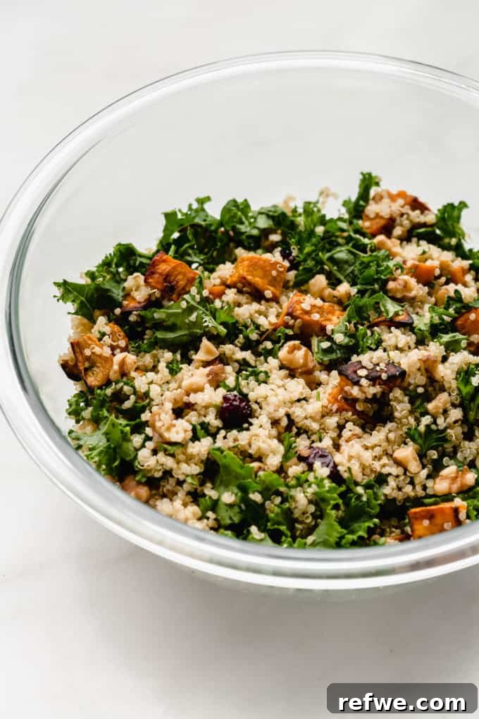 A clear mixing bowl showing the Quinoa and Kale Salad with Sweet Potatoes, after being thoroughly mixed with the dressing