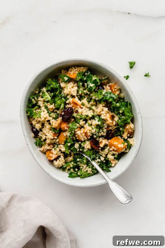 A beautifully presented bowl of quinoa kale salad with sweet potatoes, placed on a white bowl with a white napkin beside it