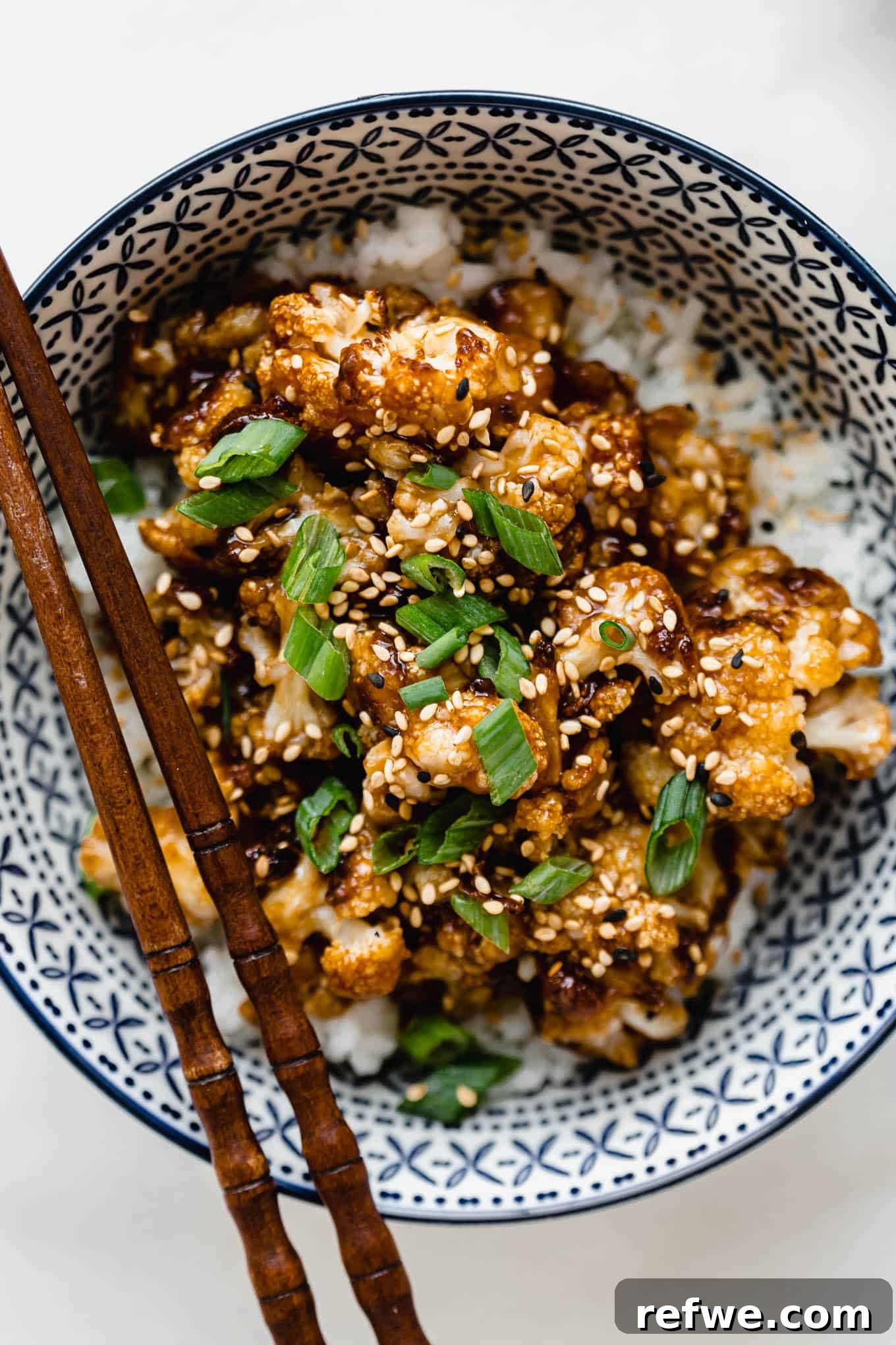 Spicy Peanut Kung Pao Cauliflower 2 Roasted Kung Pao cauliflower with sauce, garnished with green onions in a vibrant blue bowl, ready to be served.