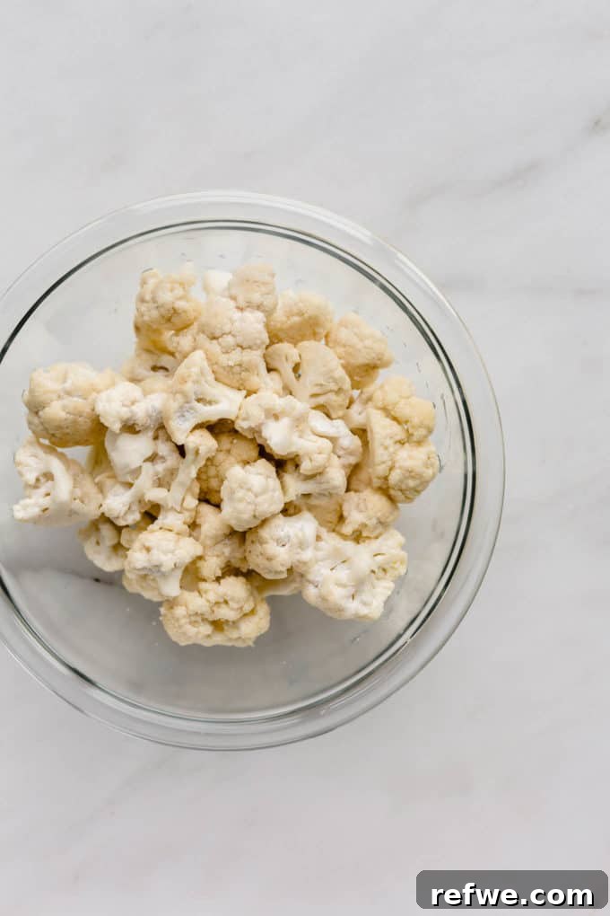 Spicy Peanut Kung Pao Cauliflower 3 Cauliflower florets in a white mixing bowl, lightly coated with oil and cornstarch.