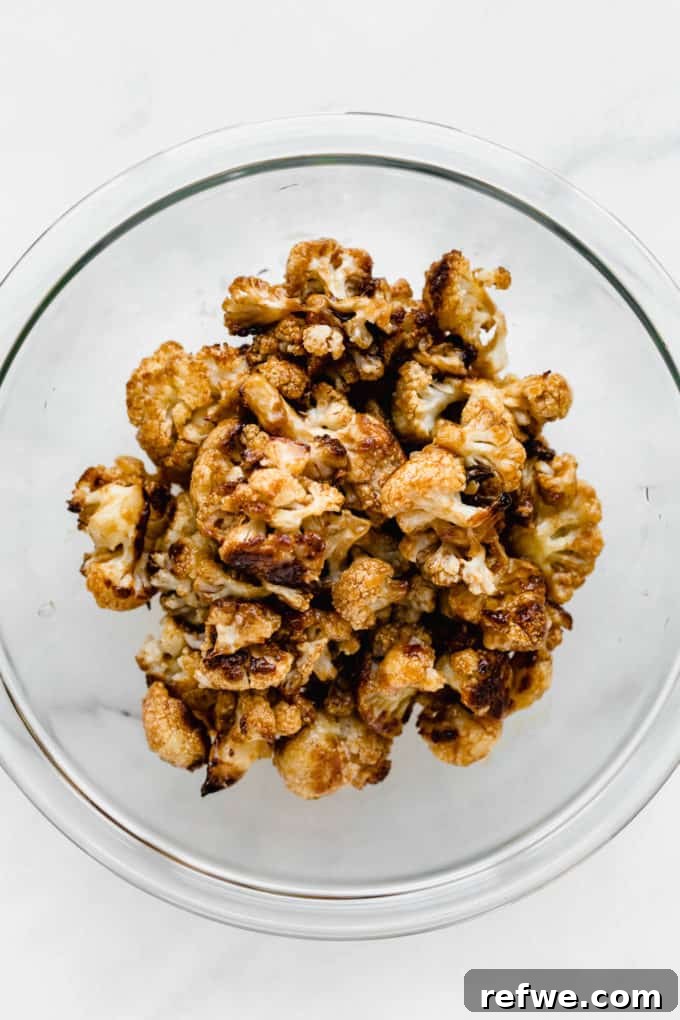Spicy Peanut Kung Pao Cauliflower 5 Roasted cauliflower being tossed with Kung Pao sauce in a clear mixing bowl, showing even coating.