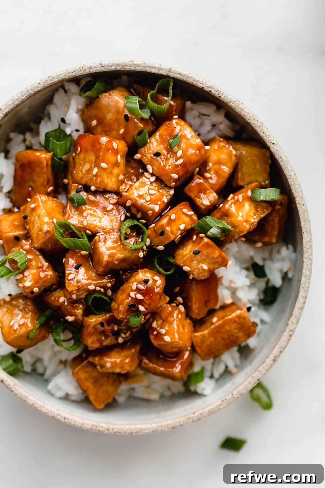 Caramelized Tofu 9 A bowl filled with rice and sweet and sour tofu topped with sliced green onions