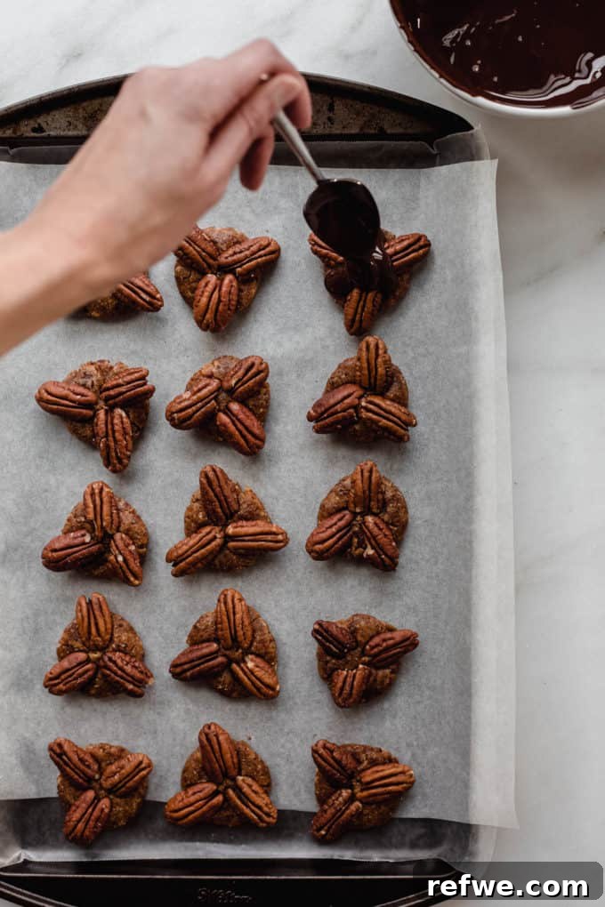 Wholesome Chocolate Turtles 7 A hand drizzling rich melted dark chocolate over a tray of healthy date and pecan candies