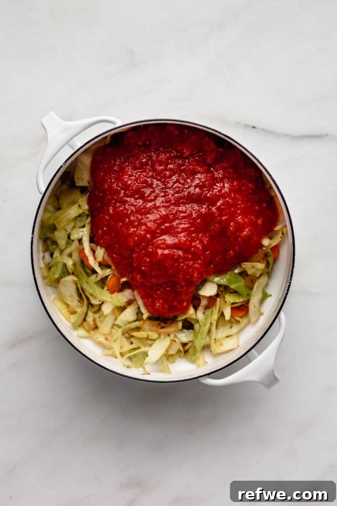 Hearty Vegetarian Cabbage Soup 4 Shredded cabbage, mixed vegetables, and crushed tomatoes combined in a white pot, ready for simmering
