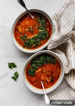 Two bowls of cabbage soup topped with parsley and a striped beige napkin on the side