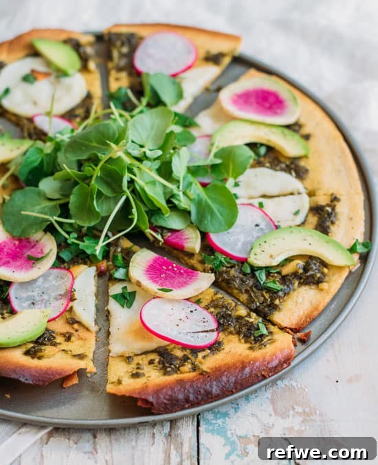 slice of chickpea crust pizza with melted vegan cheese, pesto, and fresh toppings