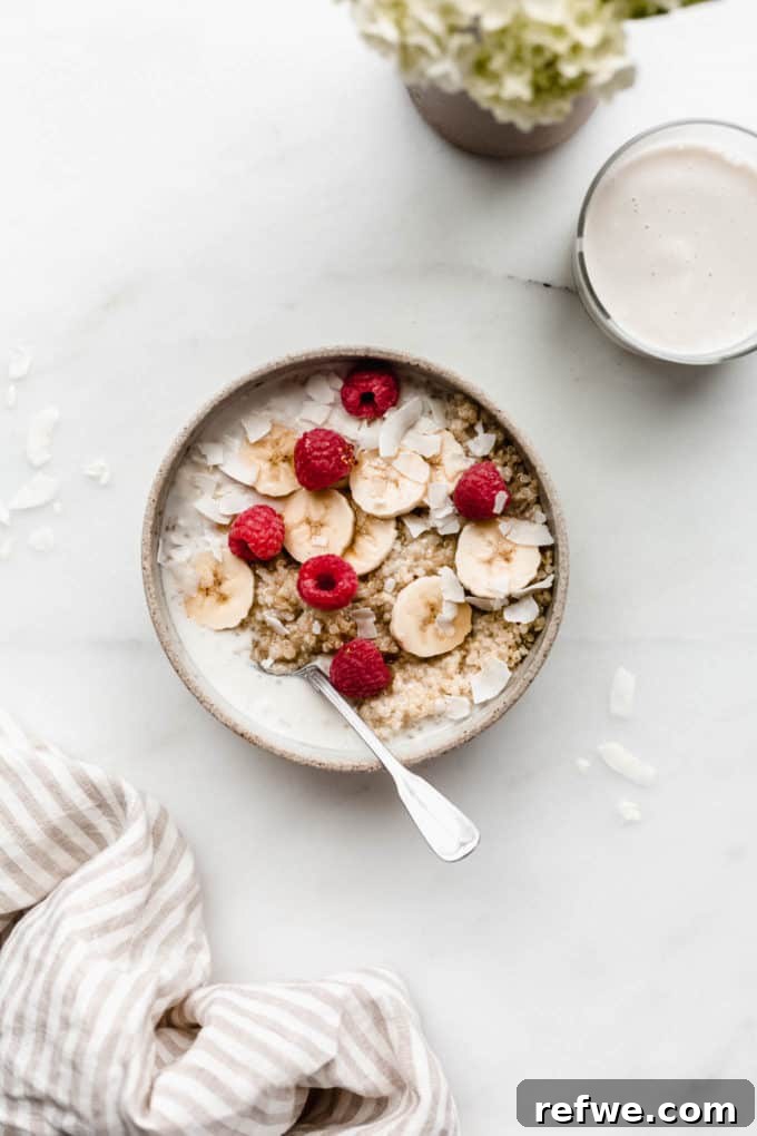 Morning Quinoa Nourishment 2 A vibrant breakfast quinoa bowl topped with sliced bananas, fresh berries, and shredded coconut, accompanied by a glass of milk and decorative flowers, highlighting a healthy morning meal.