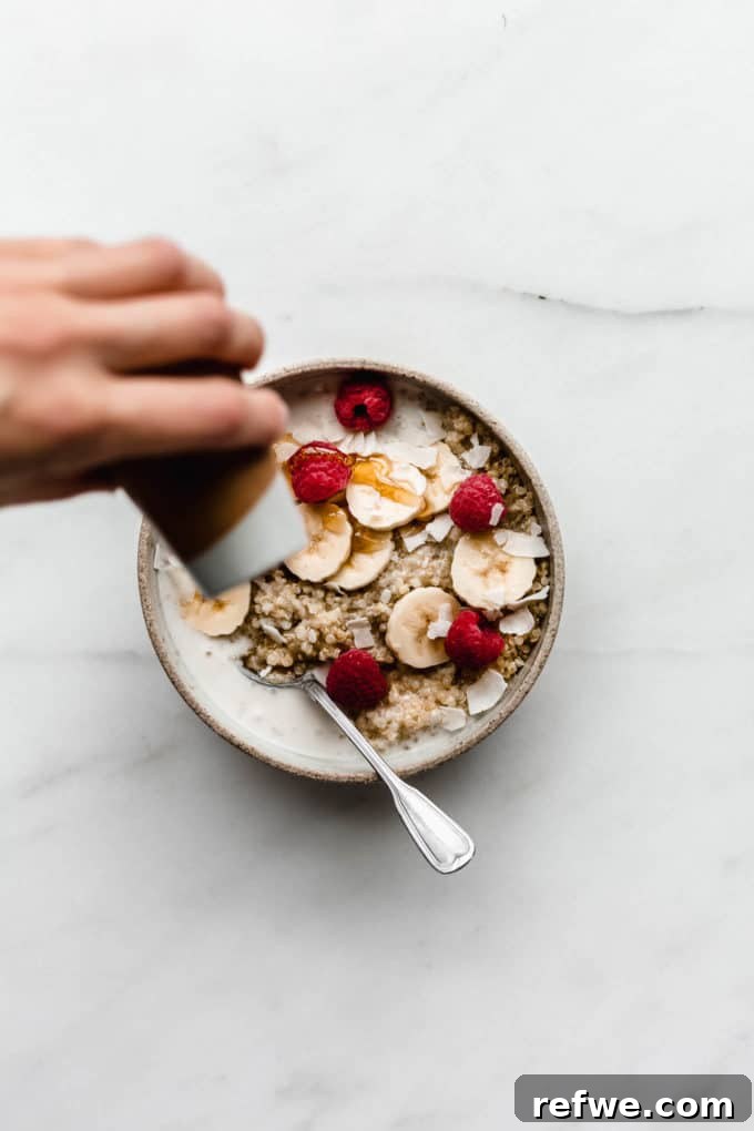 Morning Quinoa Nourishment 4 A hand gently drizzling golden maple syrup over a freshly prepared bowl of breakfast quinoa, adding a touch of natural sweetness.