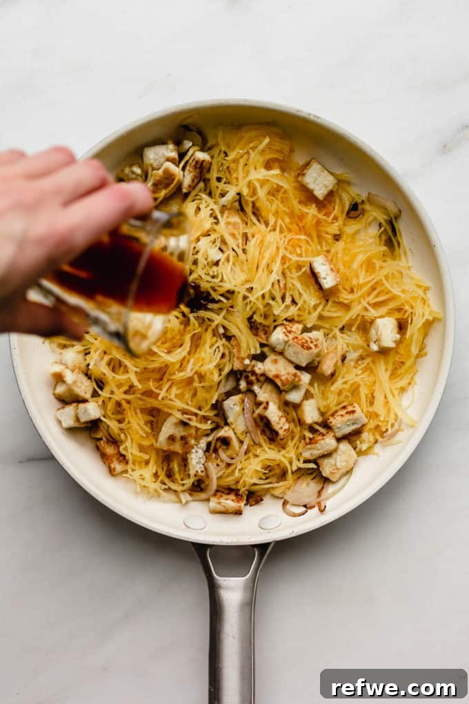 Squash Noodle Pad Thai 5 A hand pouring homemade Pad Thai sauce into a pan filled with spaghetti squash and tofu