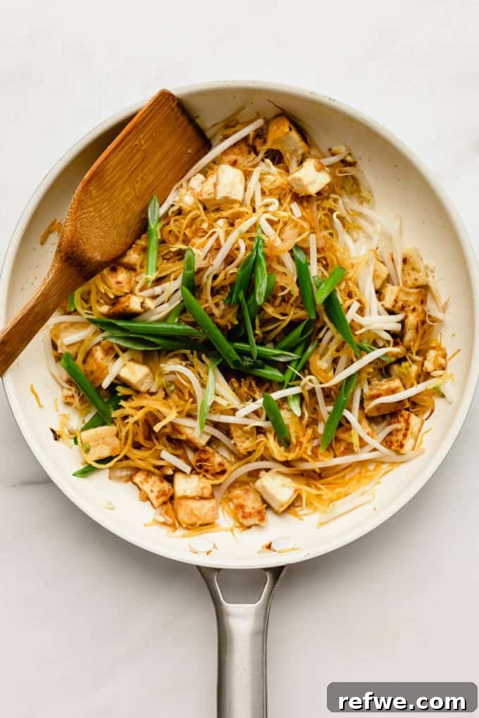 Squash Noodle Pad Thai 6 A white pan with spaghetti squash, tofu, and fresh green onions mixing together