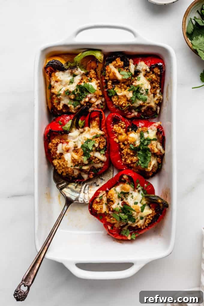 Wholesome Quinoa & Veggie Stuffed Peppers 4 quinoa stuffed peppers in a white baking dish with a serving spoon