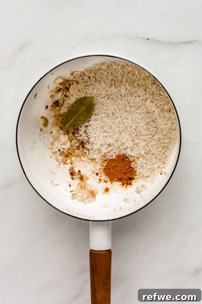 Golden Turmeric Rice 4 A white pot containing shallots, garlic, uncooked rice, turmeric powder, pepper, and a bay leaf, mixed together before liquid is added