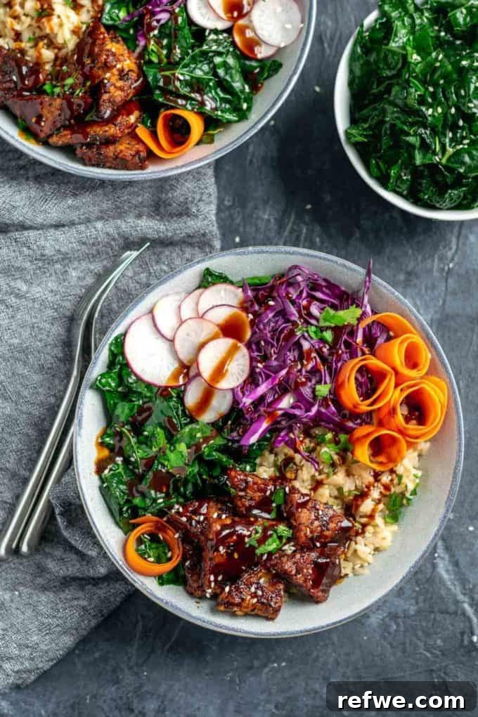 Unlock Tempeh's Potential 23 Recipes and a Full Cooking Guide 7 A white bowl featuring sticky Hoisin Glazed Tempeh served over brown jasmine rice with sesame massaged kale and fresh, crunchy vegetables.