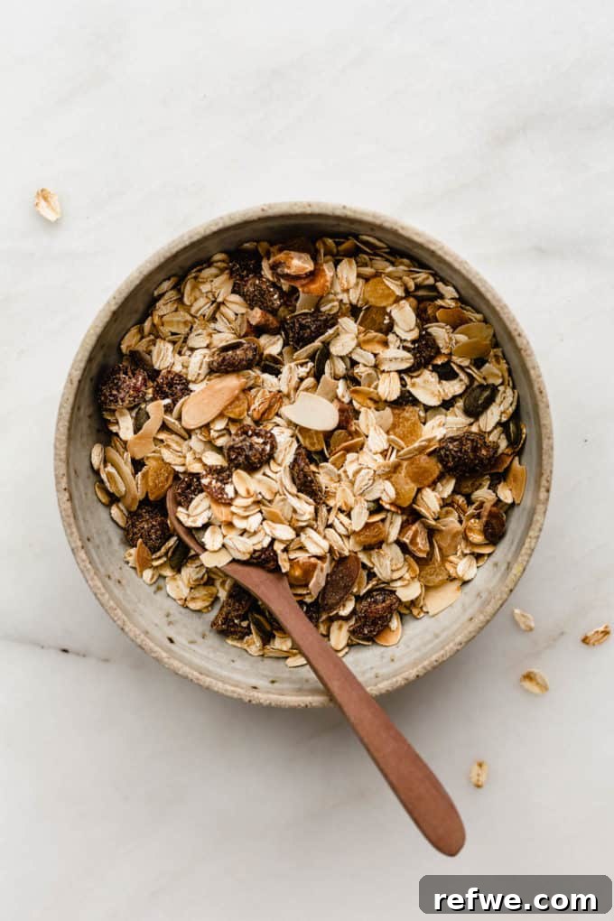 Effortless Wholesome Muesli 2 A bowl of muesli with a wooden spoon in it, showcasing a mix of oats, nuts, seeds, and dried fruits