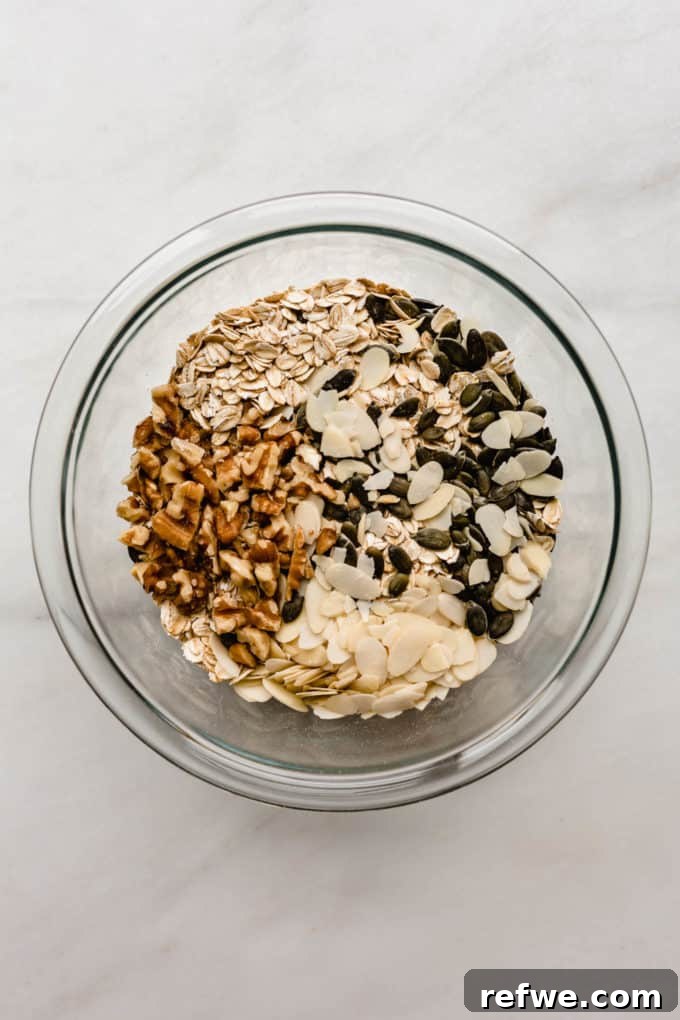 Effortless Wholesome Muesli 3 Walnuts, almonds, pumpkin seeds, and rolled oats in a clear mixing bowl, ready for toasting