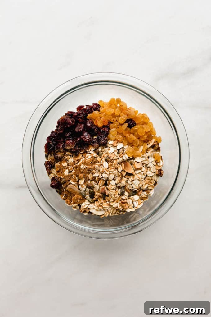 Effortless Wholesome Muesli 5 Toasted oats, nuts, dried cranberries, and golden raisins in a clear mixing bowl, ready to be tossed