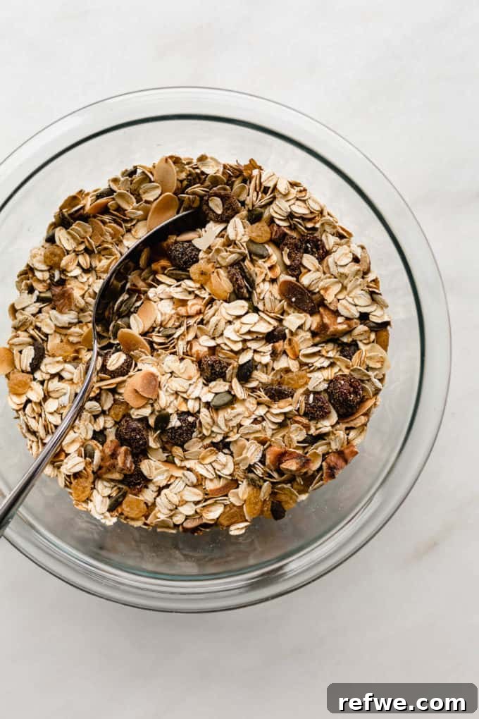 Effortless Wholesome Muesli 6 A clear mixing bowl filled with freshly toasted muesli, featuring a blend of oats, nuts, seeds, and dried fruits