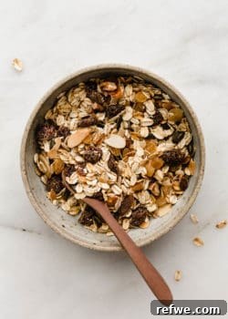 A bowl of muesli with a wooden spoon in it, showcasing a mix of oats, nuts, seeds, and dried fruits