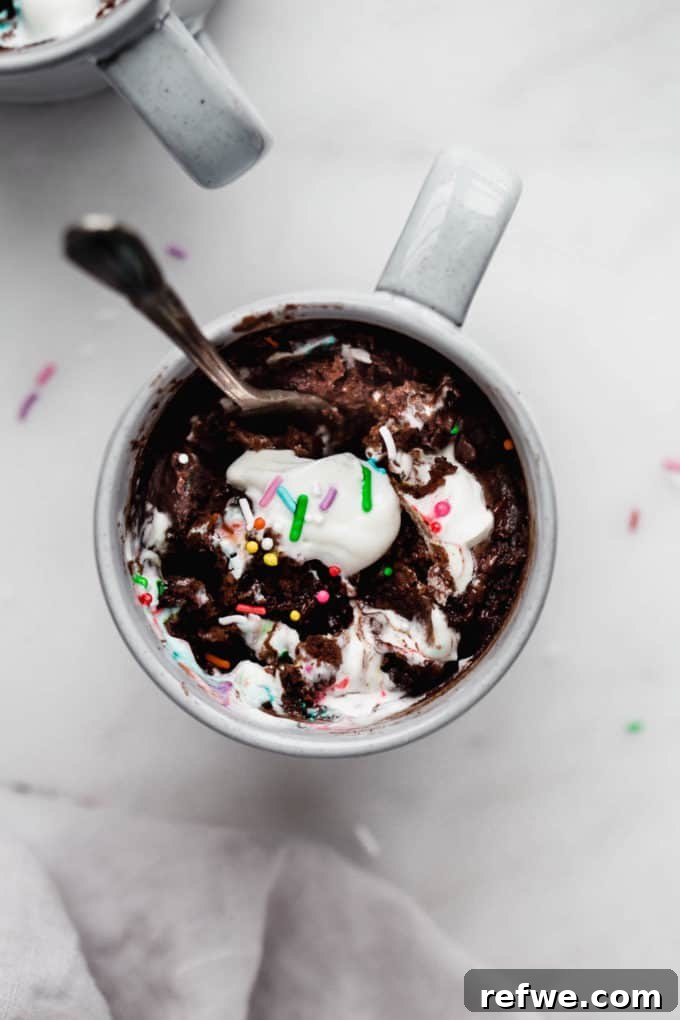 A chocolate mug cake with fluffy whipped cream and colorful sprinkles on top, ready to be enjoyed.