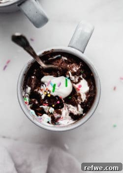 A chocolate mug cake with whipped cream and sprinkles on top