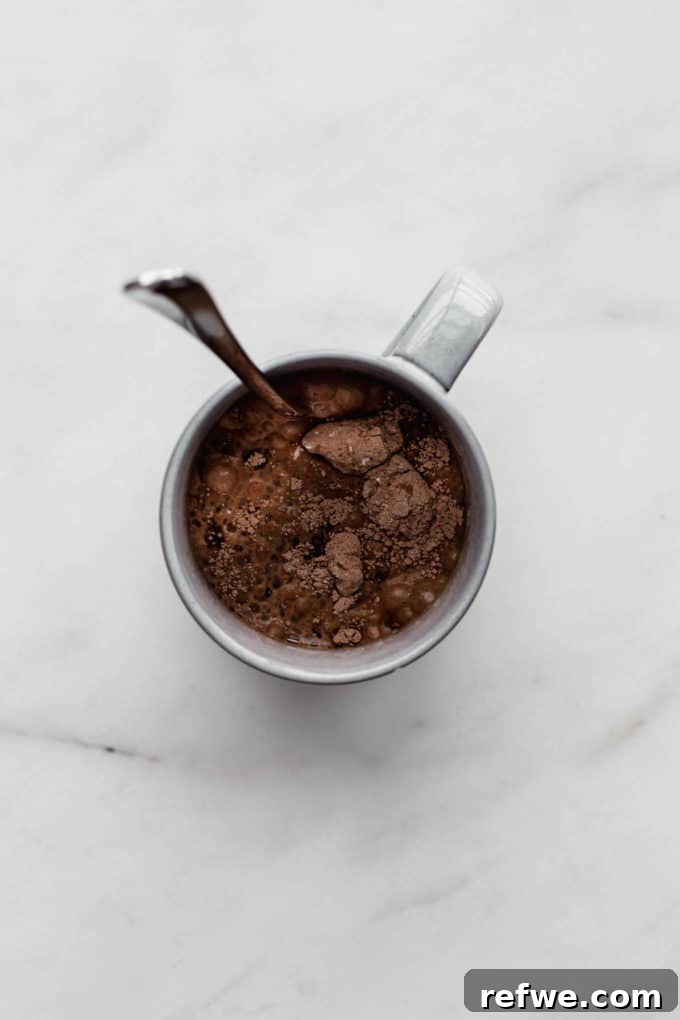 A grey mug containing raw, unbaked batter for a chocolate mug cake, ready for the microwave.