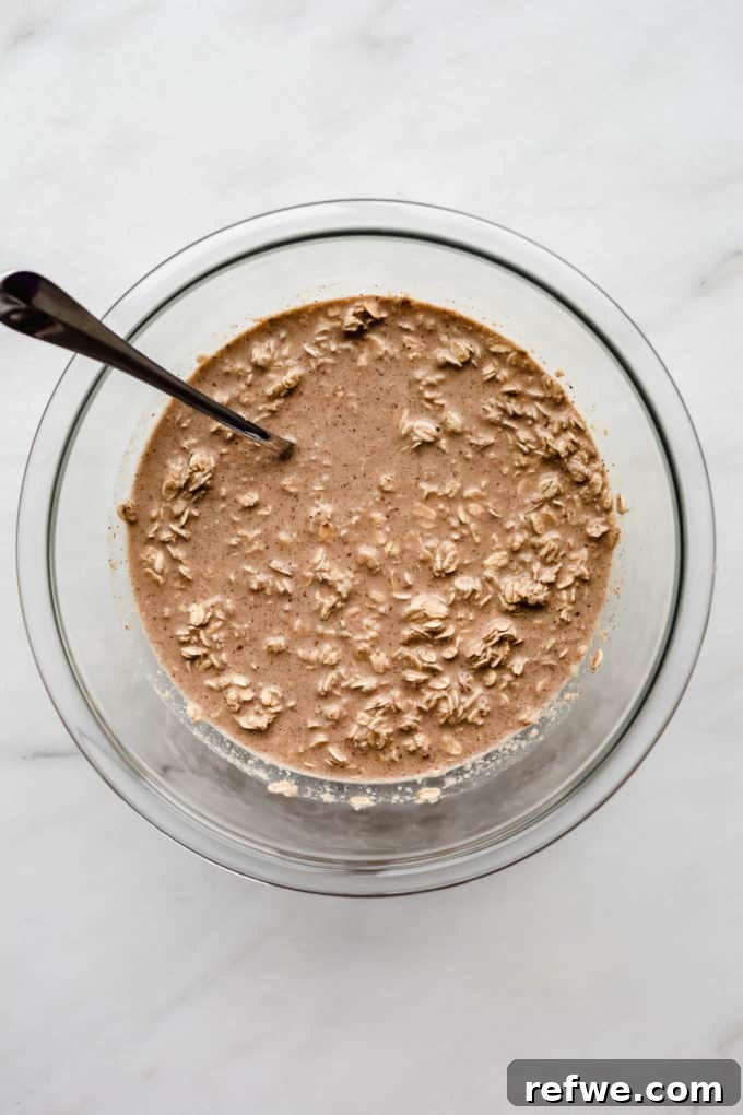 A clear mixing bowl showing the combined wet and dry ingredients for baked oatmeal, creating a thick batter.