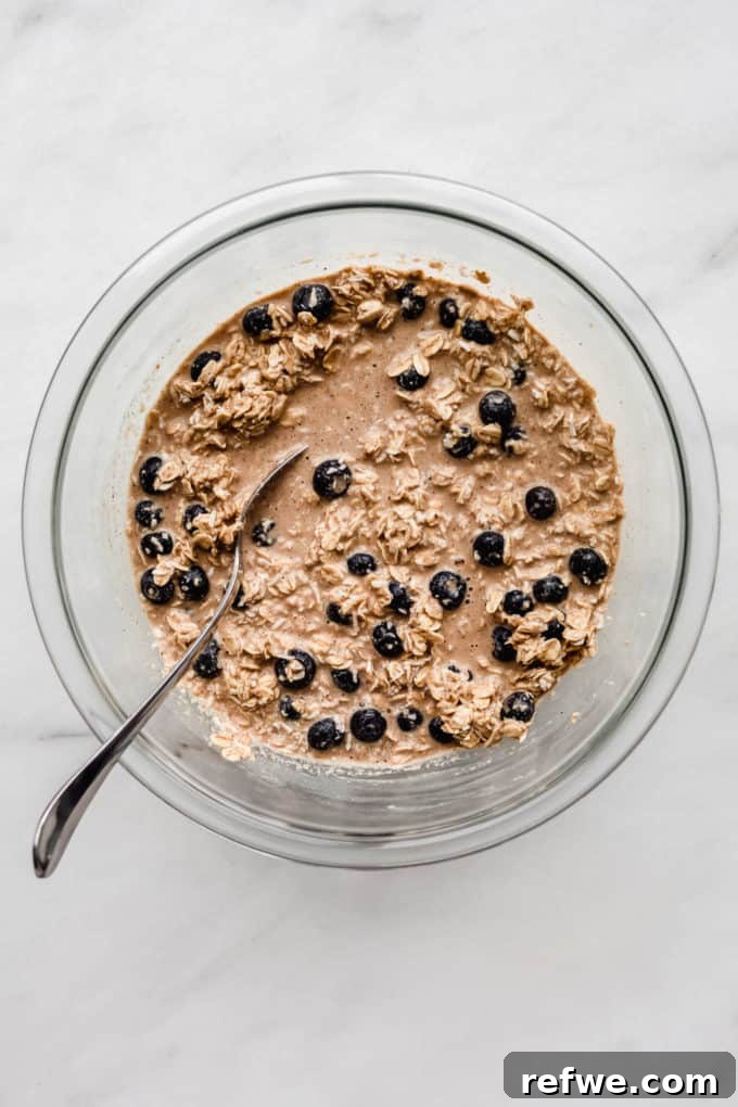A clear mixing bowl with the finished baked oatmeal batter, showing oats and blueberries thoroughly mixed.