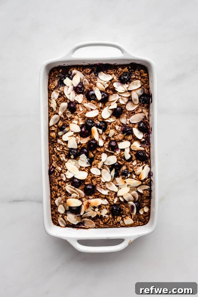 Baked oatmeal in a white square baking dish, topped with blueberries and a golden brown crust, fresh out of the oven.