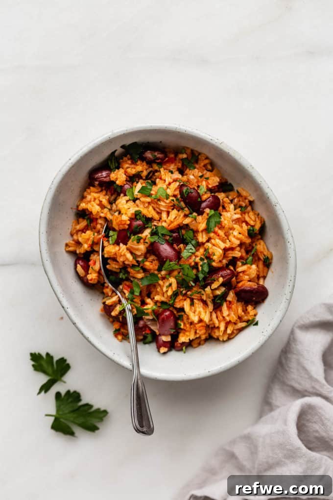 Classic Spanish Red Beans and Rice 2 A bowl of Spanish rice and beans with a spoon in it and a napkin on the side, garnished with fresh herbs