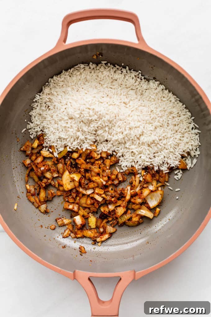 Classic Spanish Red Beans and Rice 4 A pan with onions, garlic, and white rice added, being stirred together