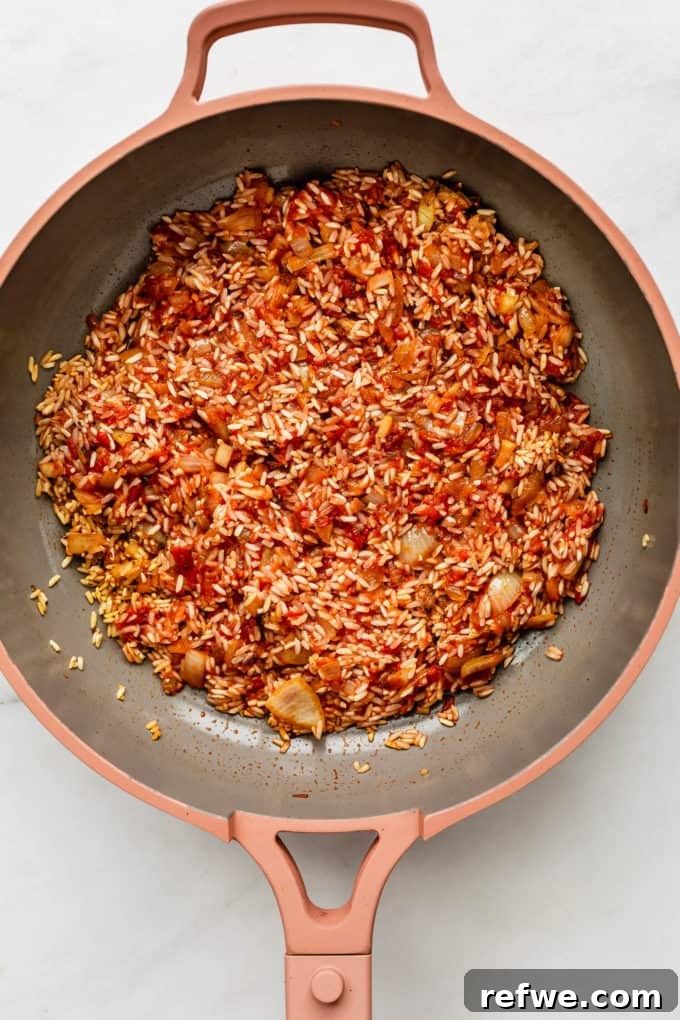 Classic Spanish Red Beans and Rice 5 A pan with crushed tomatoes, rice, onions, and spices being mixed
