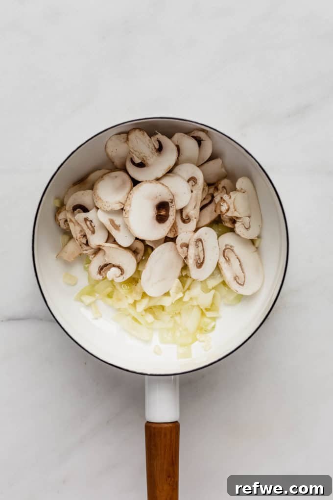 Plant-Powered Mushroom Stroganoff 4 Onions and sliced mushrooms beginning to sauté in a white pot, preparing to brown.