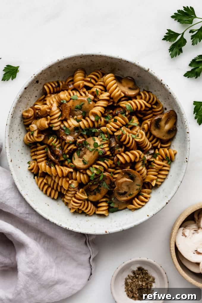 Plant-Powered Mushroom Stroganoff 10 A beautifully plated bowl of mushroom stroganoff, garnished with fresh parsley, alongside a grey napkin for an inviting presentation.