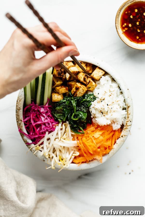 A person holding a bowl of Vegan Bibimbap with chopsticks, showing the vibrant colors and textures of the dish.