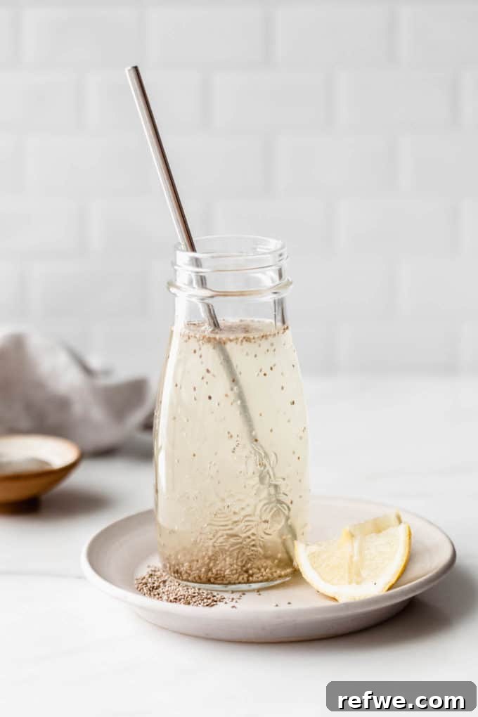 Cool Chia Quench 2 A vibrant Chia Fresca in a clear glass jar, garnished with fresh lemon slices, resting on a white plate. The background suggests a bright, natural setting, highlighting the drink's refreshing appeal.