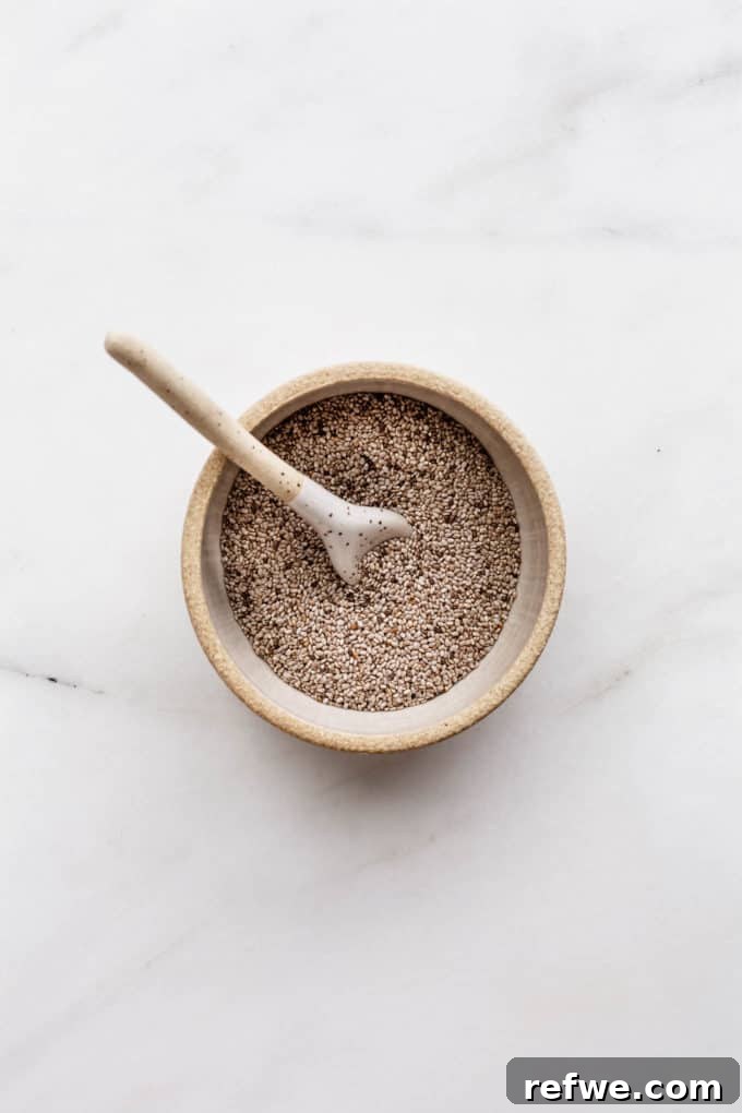 Cool Chia Quench 3 A small ceramic bowl filled with an abundance of tiny white chia seeds, showcasing their uniform texture and subtle sheen, ready to be transformed into a healthy beverage or meal.