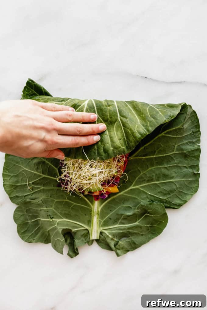 Vibrant Garden Collard Wraps 7 A hand expertly folding a collard green leaf, tucking in vegetables and hummus to form a tight wrap.