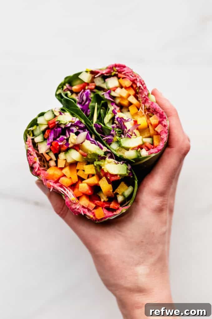 Vibrant Garden Collard Wraps 9 A hand holding a vibrant rainbow collard green wrap, sliced in half to reveal the colorful fresh fillings inside, ready to be enjoyed.