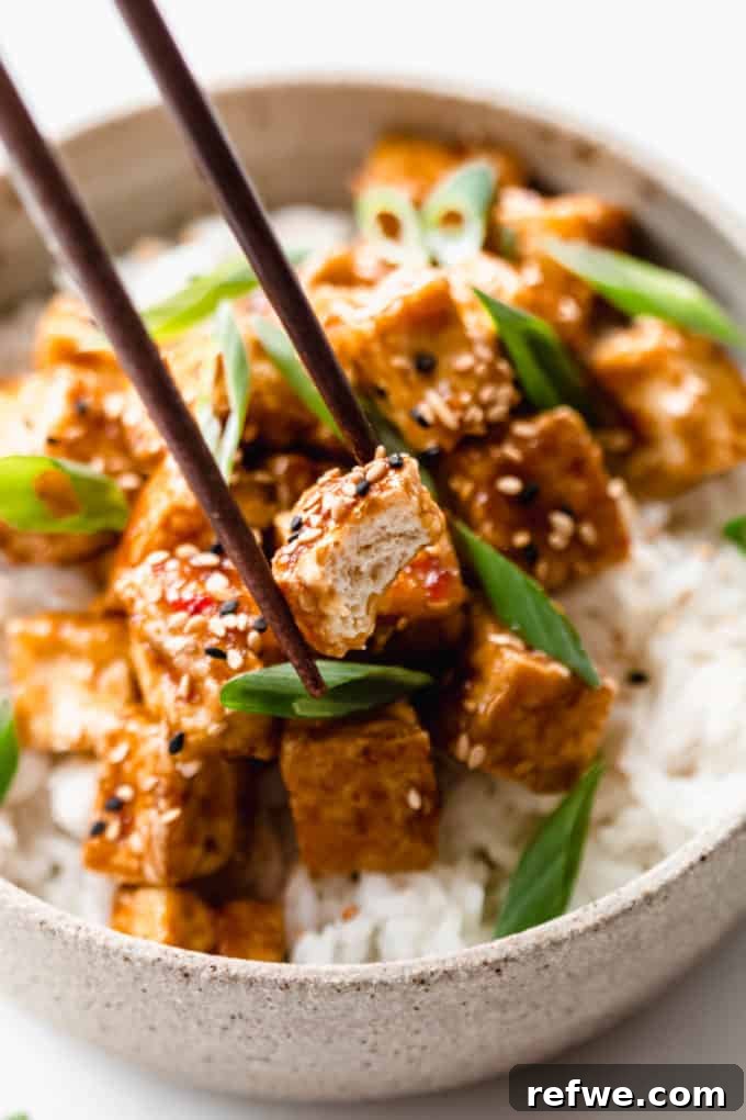 Sticky Teriyaki Glazed Crispy Tofu 8 chopsticks picking up a cube of teriyaki tofu