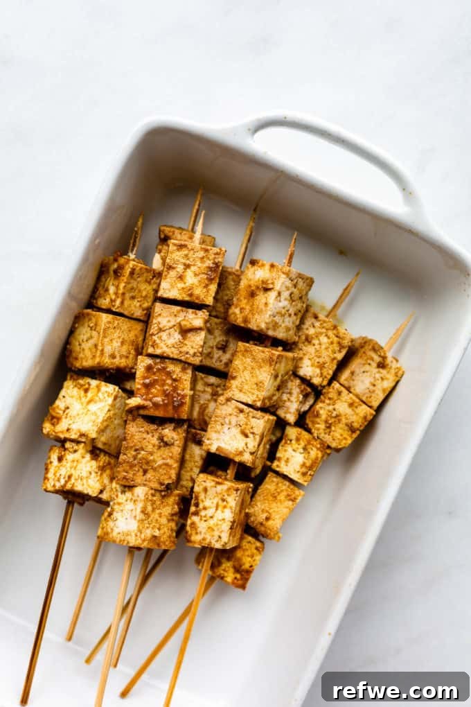 Grilled Tofu Satay with Creamy Peanut Sauce 5 Uncooked tofu satay skewers neatly arranged in a white baking dish, prepared for grilling or baking.