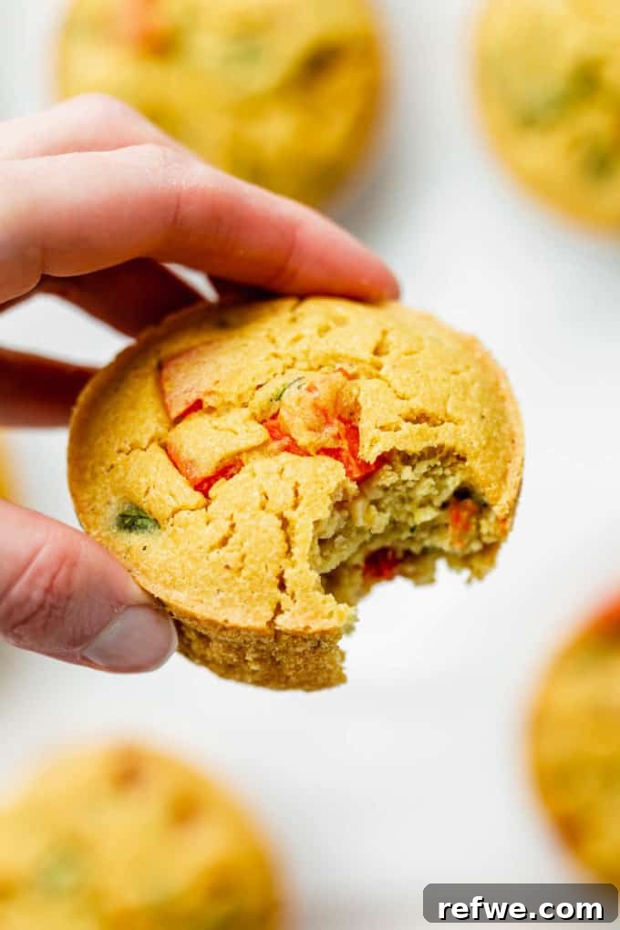 A hand holding a golden-brown chickpea flour mini quiche, showcasing its fluffy texture and savory fillings.