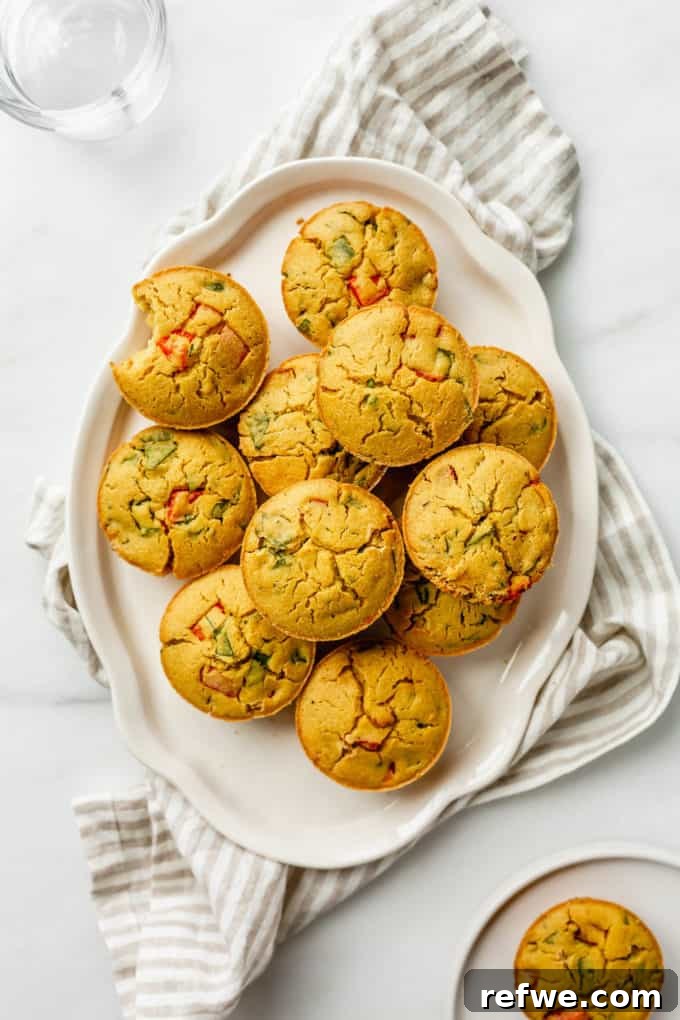A stack of perfectly baked golden chickpea flour mini quiches resting on a pristine white platter over a striped napkin, ready to be served.