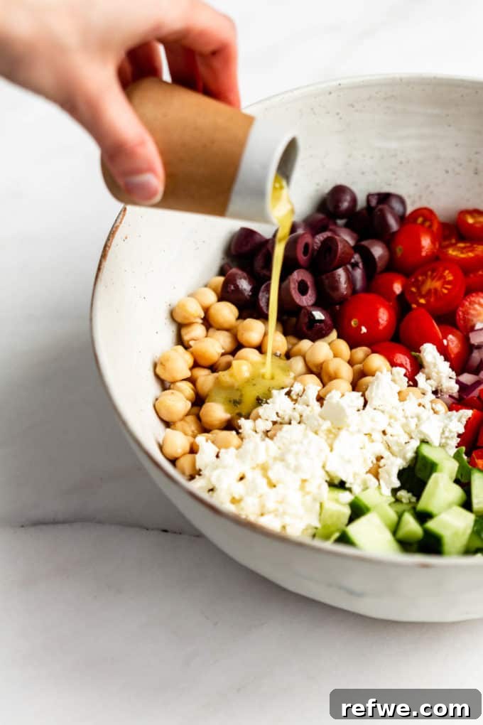 Vibrant Mediterranean Chickpea Salad 4 A hand gently pouring a homemade dressing over a bowl brimming with vibrant chickpea salad ingredients.