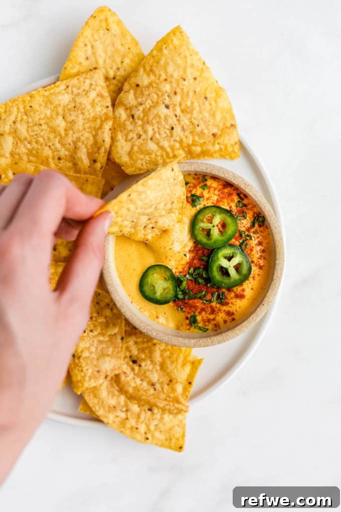 Ultimate Dairy-Free Queso 6 A hand enthusiastically dipping a golden tortilla chip into a generously filled bowl of creamy vegan queso.