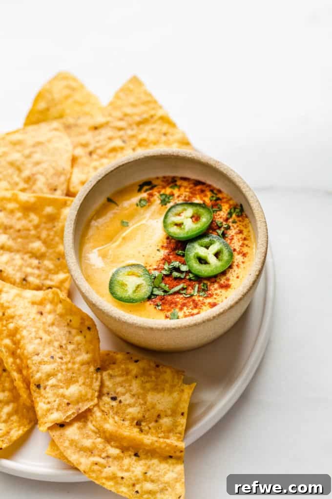 Ultimate Dairy-Free Queso 8 A small, inviting bowl of golden vegan queso is perfectly positioned alongside a pile of crisp tortilla chips, ready for dipping.