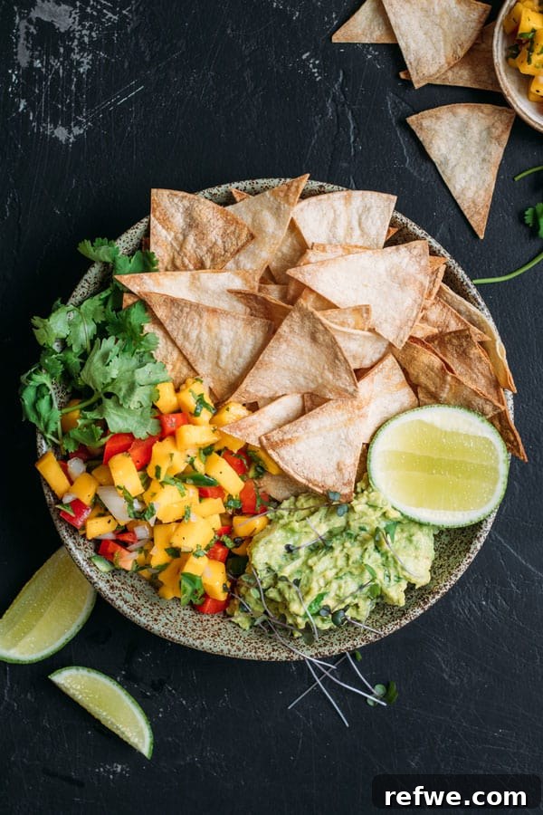 Sun-Kissed Guacamole, Mango Salsa and Crispy Baked Tortilla Chips 2 Crispy baked corn chips with fresh guacamole and vibrant mango salsa on a wooden board