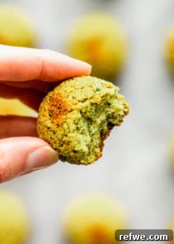 A hand holding a baked falafel ball with a bite taken out of it